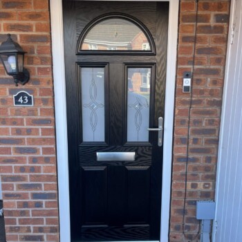 A black door with glass and a light on the outside.