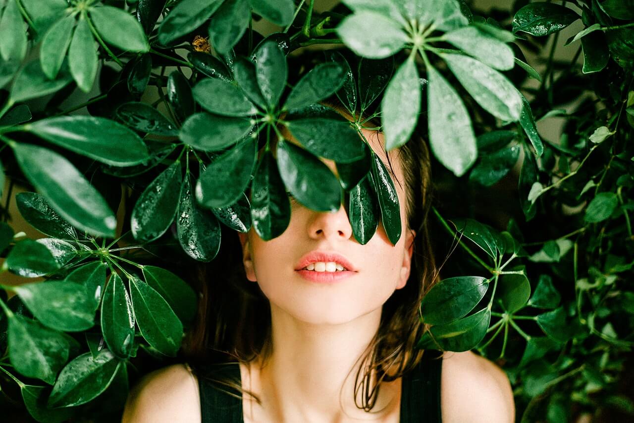 about-bg-2 A woman with her eyes closed surrounded by green leaves.